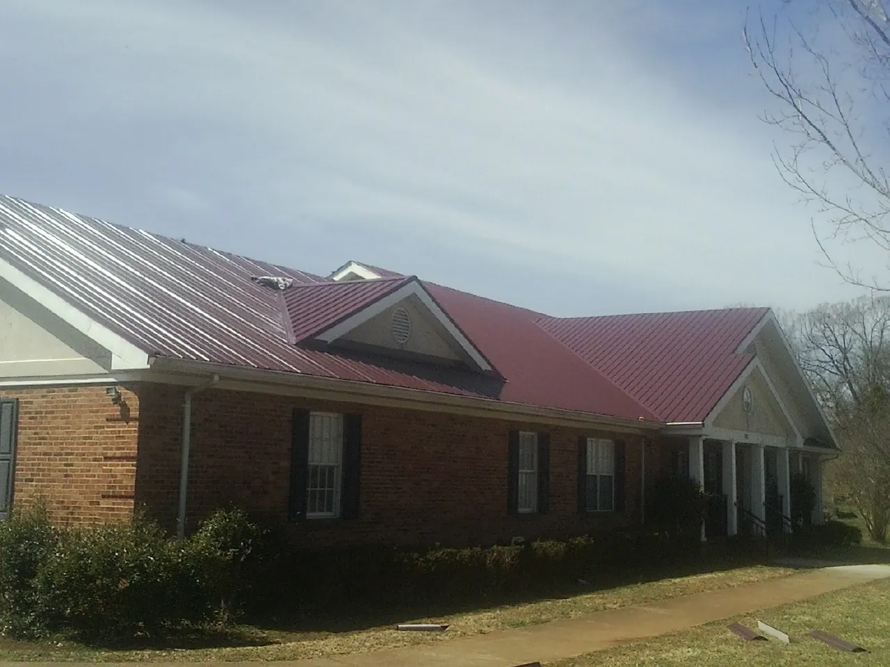 Red metal roof with gabled entries on a long brick building, from a Hail Damage Roof Repair job in West Lebanon