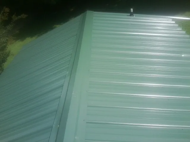New green metal panels meeting at the ridge of a roof — Flat Roof Repair work by our crew in West Lebanon