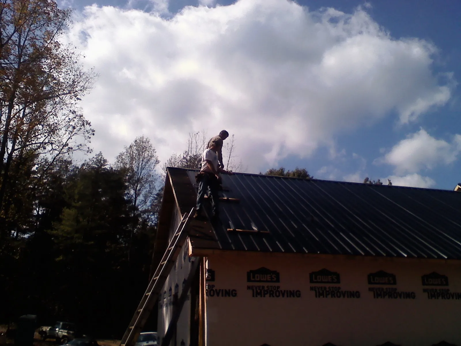 Roofer fastening dark metal panels high against a cloudy sky, from a Roof Inspection job in West Lebanon