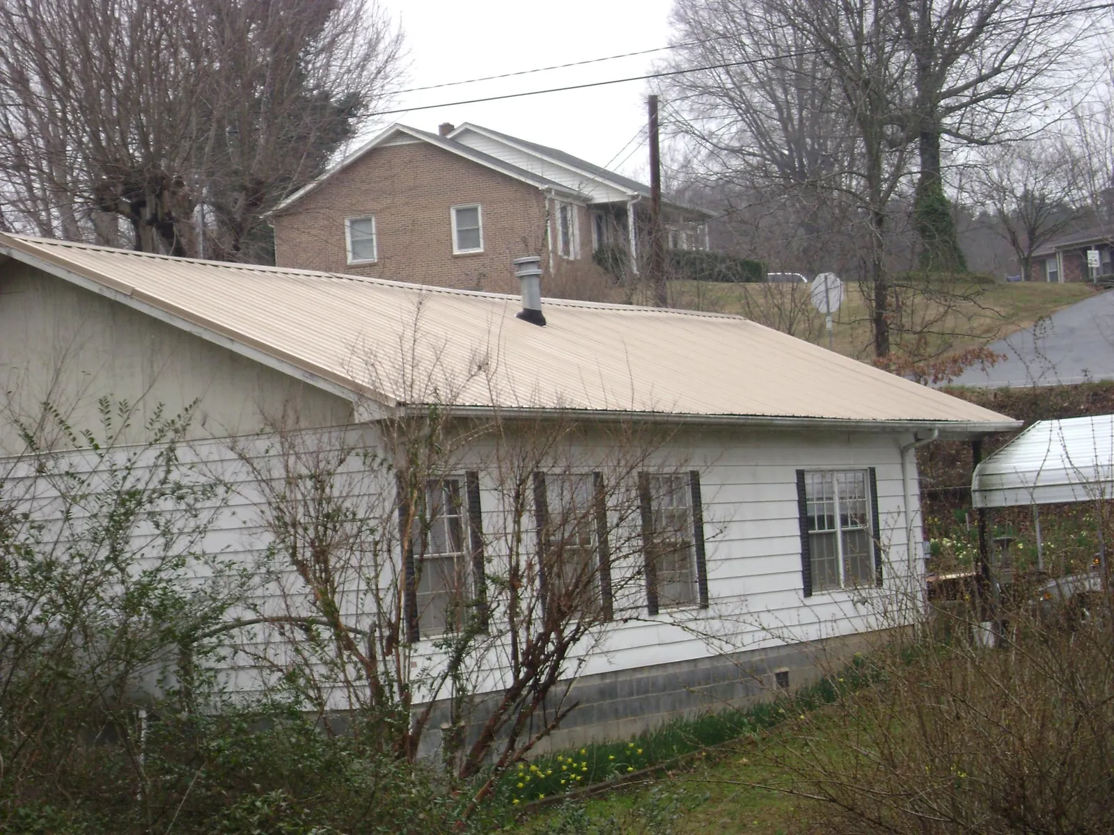 Tan metal roof on a white sided house set into a hillside — Commercial Roofing by Roofing Brothers in West Lebanon